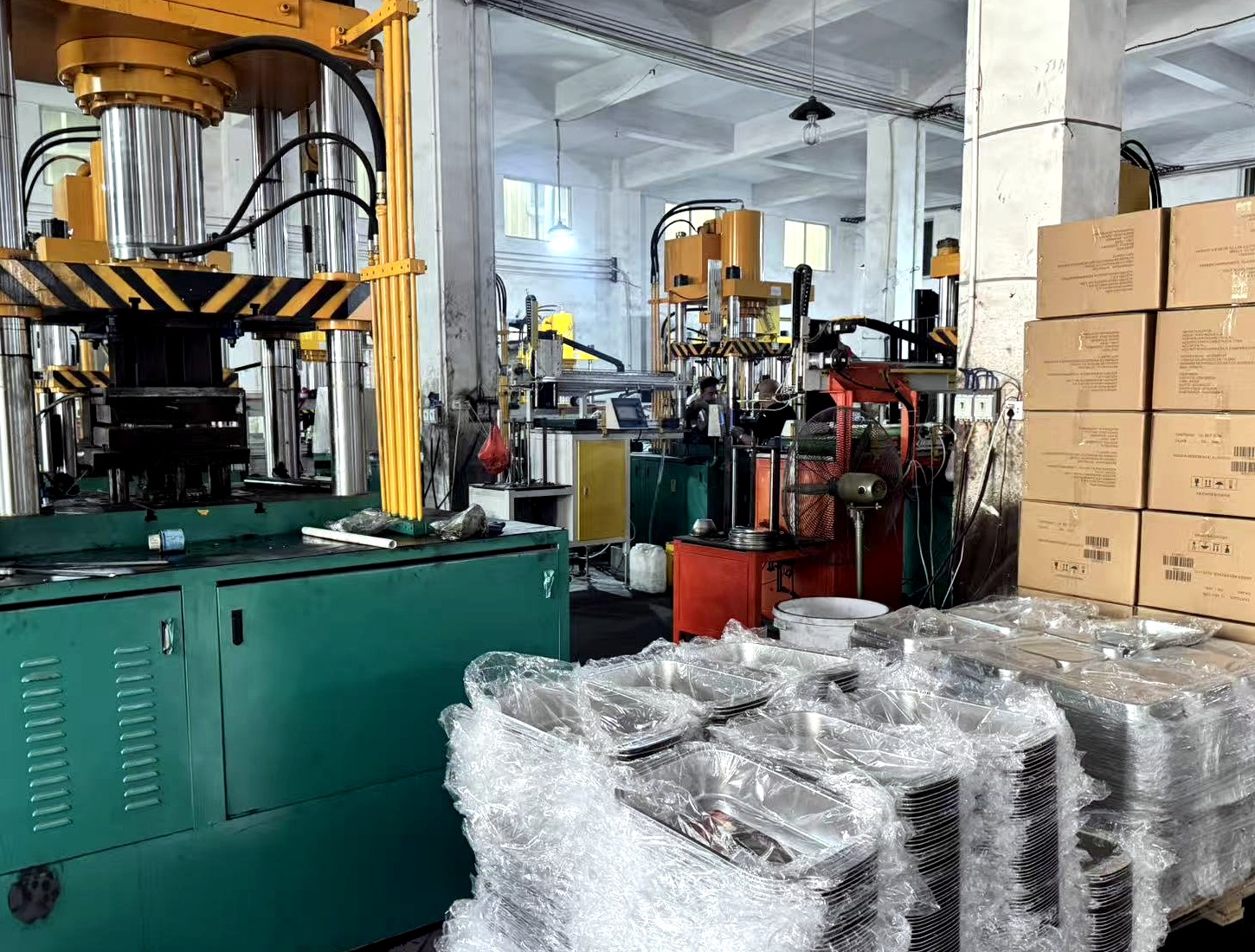 Wrapped stainless-steel food pans beside workshop equipment and stacked cartons